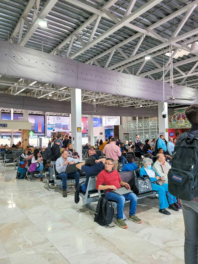 The departures lounge at Queretaro Airport full of passengers waiting for their flights and a Starbucks in the background.
