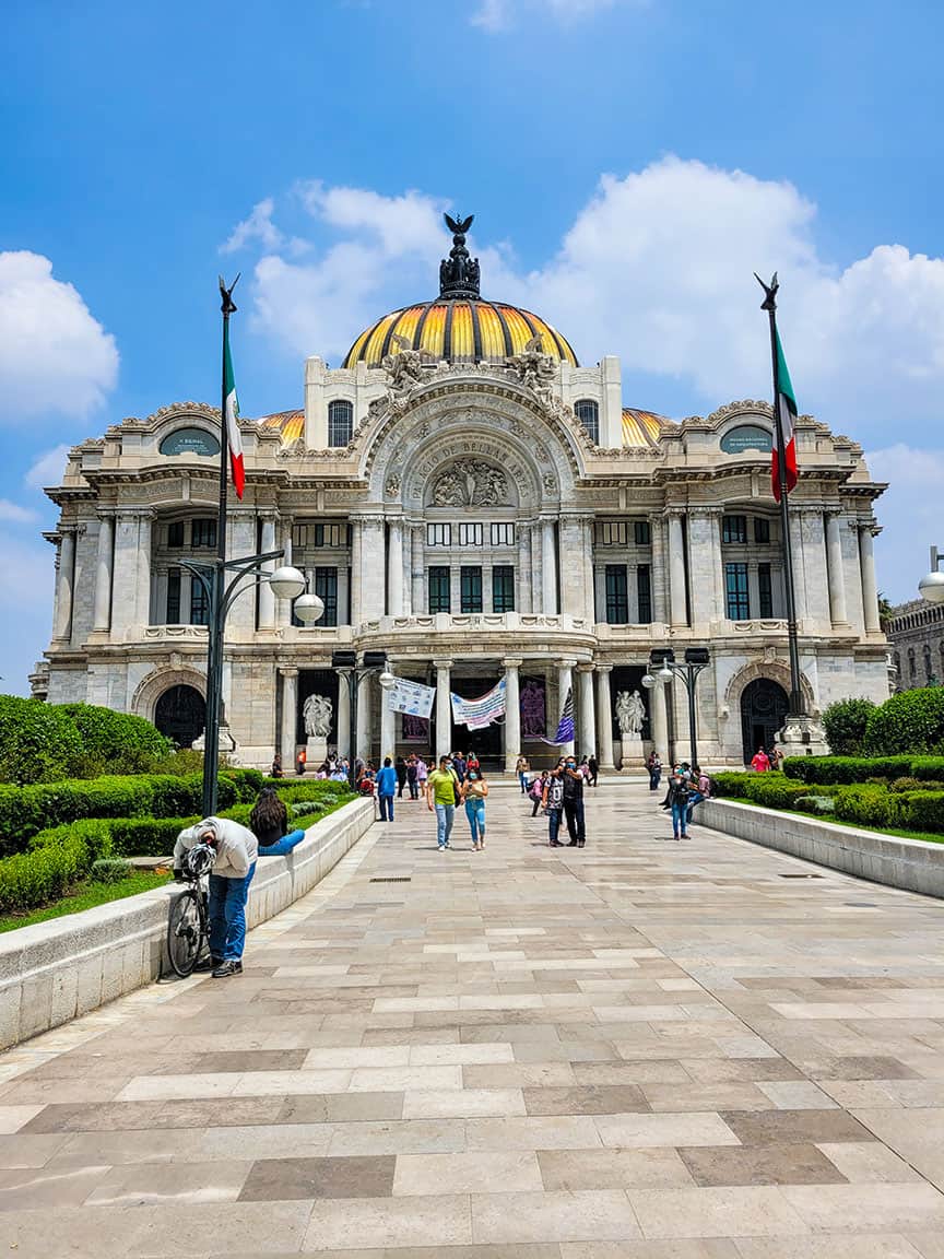 A view of the Palacio de Bellas Artes in Mexico City with blue skies over head and fluffy white clouds.