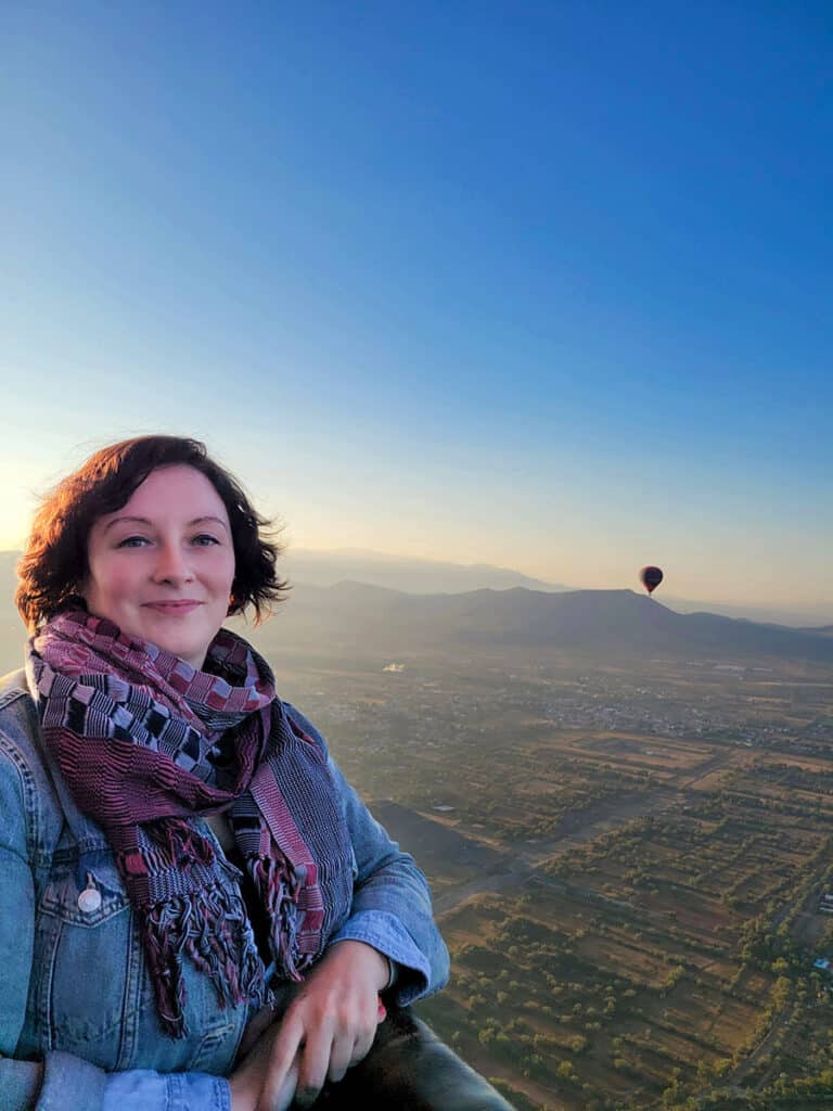 Ashlea in the hot air balloon basket over Teotihuacan at sunrise with a balloon floating in the background.