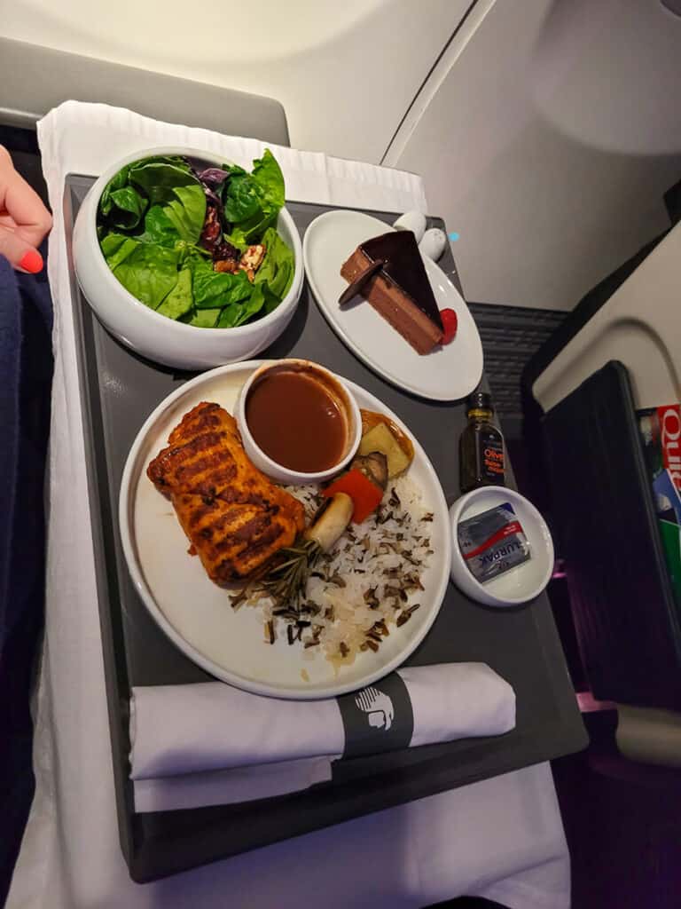 An Aeromexico Business Class meal featuring three courses with salad, tamarind chicken and chocolate cake, served on china dishes with linen tablecloth.