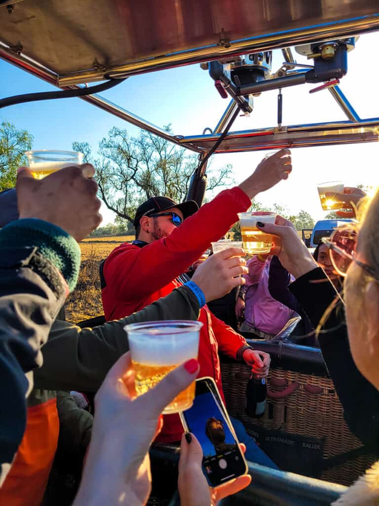 A pilot leading the champagne toast inside the basket of a landed hot air balloon.