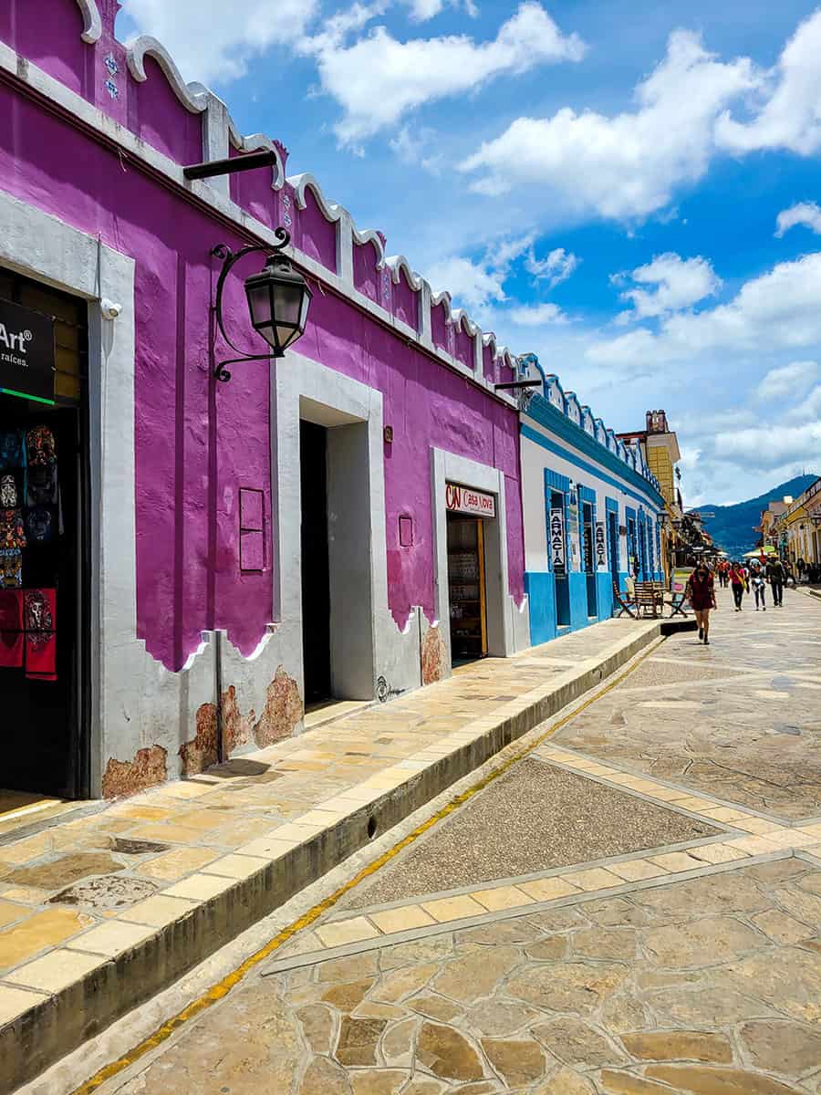 Vibrant colonial buildings on a pedestrian street in San Cristobal de las Casas with mountains in the background.