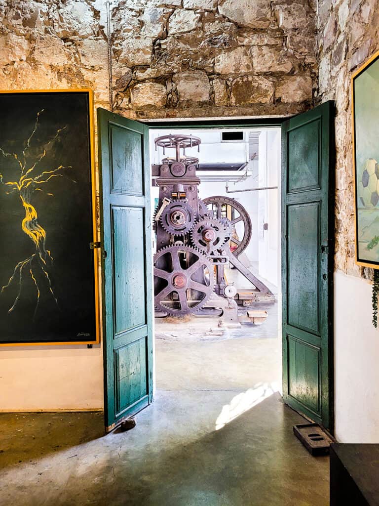 Looking through a gallery at Fabrica Aurora in San Miguel de Allende with paintings on the walls and a large printing press at the end of the space.